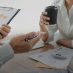 Two people are sitting at a table with papers and cups.