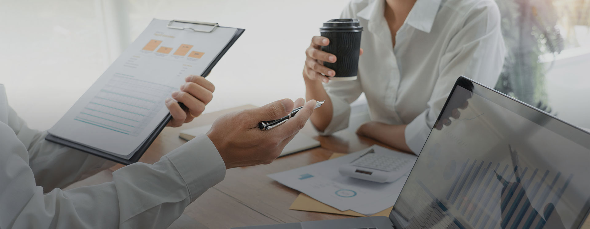 Two people are sitting at a table with papers and cups.